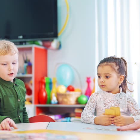 kleine mädchen während des unterrichts auf dem hintergrund des klassenzimmers mit fernsehen. grundschüler spielen mit hilfe des lehrers im unterricht ein bilderkarten-spiel.