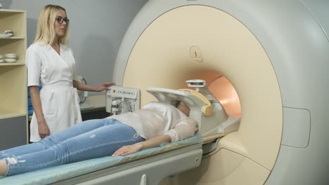 woman doctor radiologist makes brain, head, neck mri scanning. young female patient on automatic table enters into a closed-type mri machine using modern equipment, coil on the patient's head.