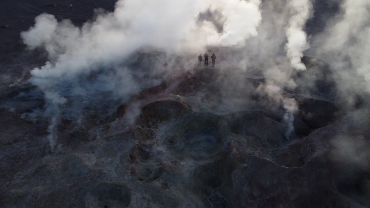aérea: turistas de pie iluminados en medio de geysers humeantes en sol de manana