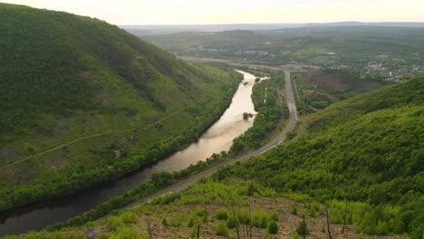 aerial reveal forward of young man hiking on a rocky cliff in pennsylvania showing the forest and river during a summer sunset