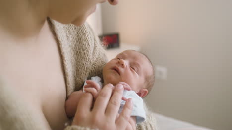 close up view of brunette woman sitting on the bed holding her baby and touching his hand