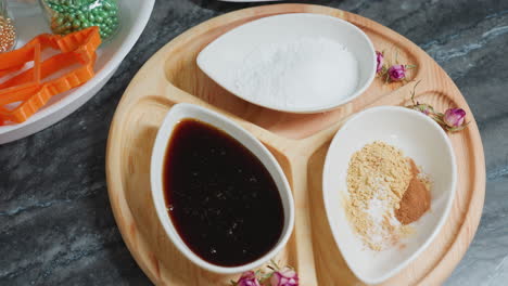 close-up of honey in ceramic bowl alongside powdered sugar and mixed spices on wooden plate, small pink flowers add decorative touch, baking ingredients and cookie cutters arranged in background