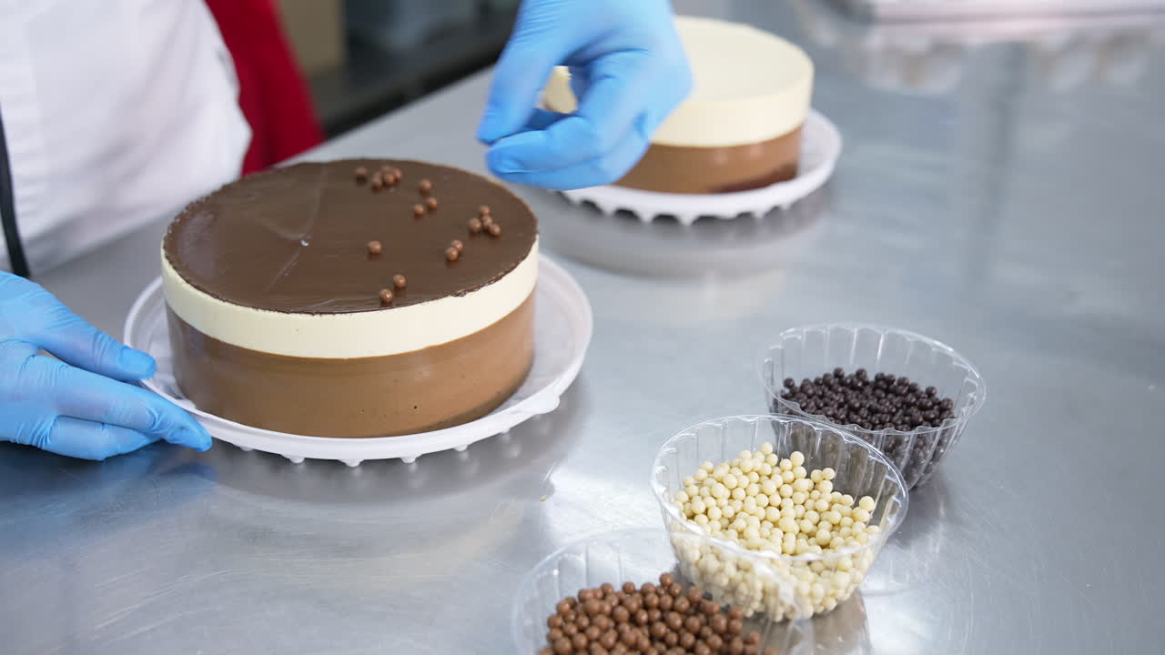Decoration of the cake at confectionary factory. Worker puts white, milky and dark chocolate beads on top of the beautiful cake. Close up.