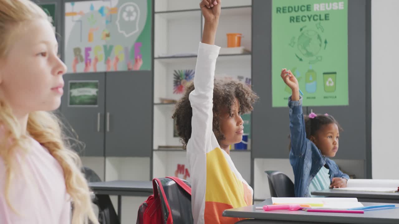 Video of diverse schoolchildren sitting at desks raising hands in class