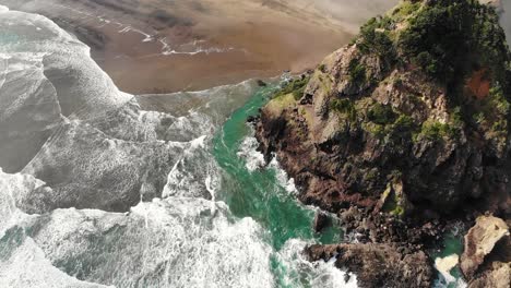 waves crash against volcanic lion rock, piha beach, new zealand