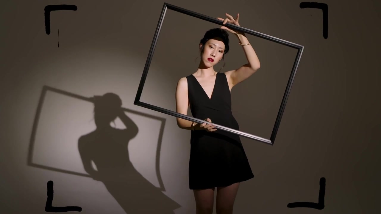 Posing Chinese woman in sleeveless black dress rotating frame in studio, spotlight casting shadow