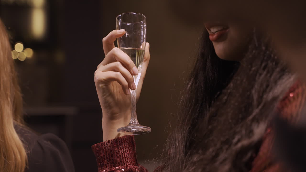vista de cerca de una chica morena con ropa elegante mientras habla con sus amigos y sostiene una copa de champán en la fiesta de año nuevo