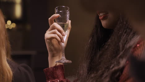 close up view of a brunette girl wearing elegant clothes while talking with her friends and holding a glass of champagne at the new year's party