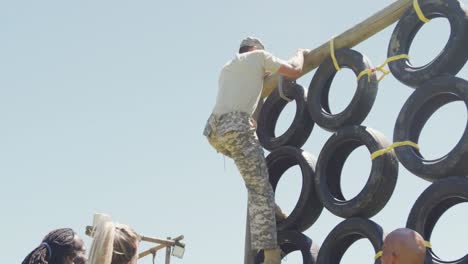 fit caucasian male soldier in combat uniform climbing tyre wall on army obstacle course in the sun