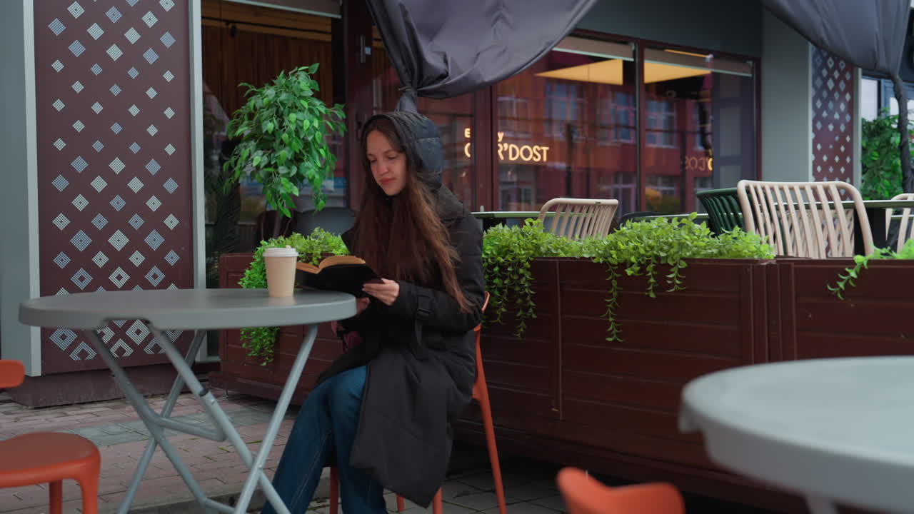 Mulher relaxando ao ar livre. Mulher navegando no celular do lado de fora. Mulher sentada no terraço de um café. Mulher aproveitando a noite em uma mesa de café no jardim. Mulher sentada calmamente em um café ao ar livre cercada por plantas e cadeiras