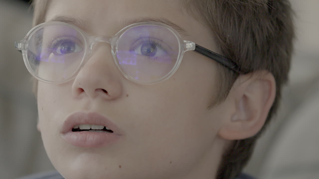 primer plano de la cara de un niño mientras reacciona a lo que está viendo en la televisión