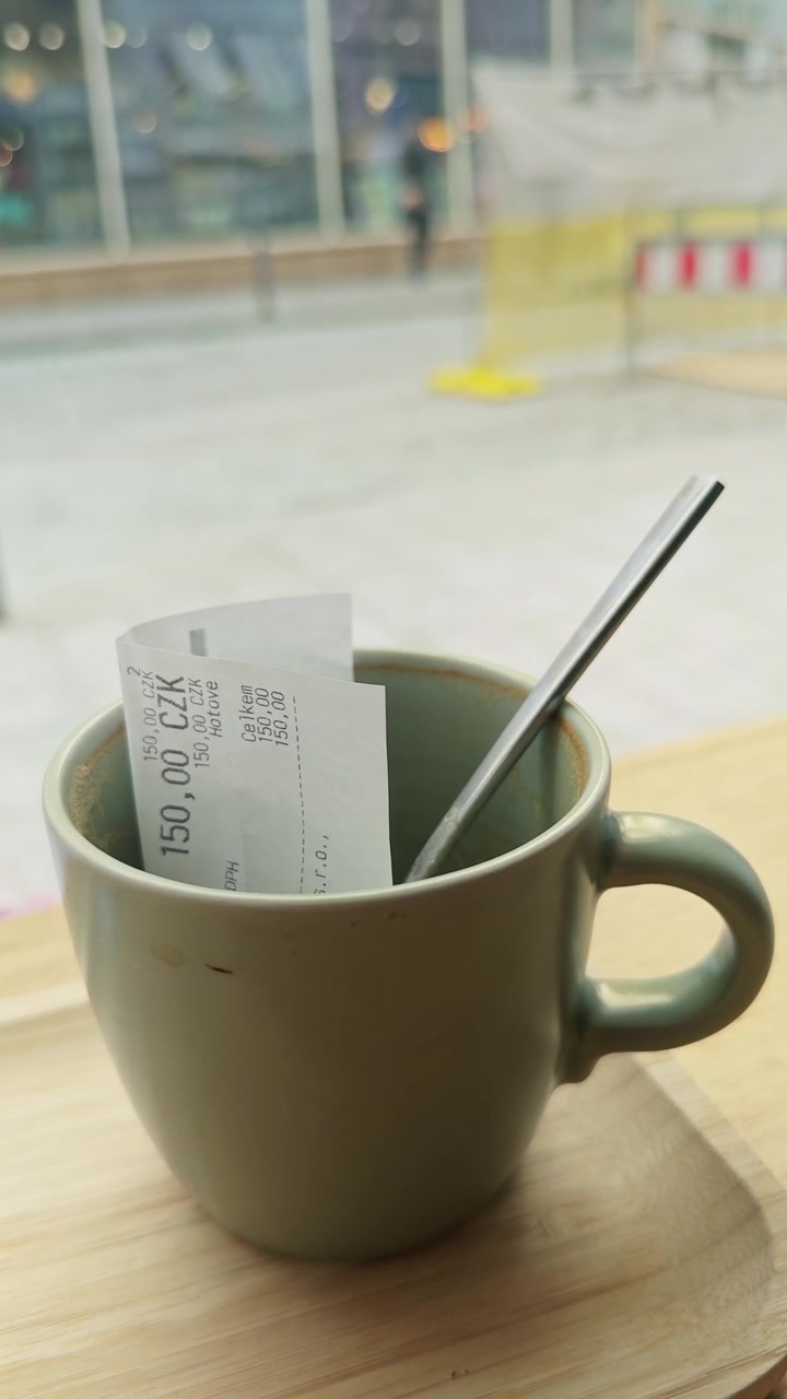 Primer plano vertical de una taza de café vacía con un recibo pagado sobre una mesa de cafetería junto a una ventana, capturando la reflexión tranquila, el estilo de vida del consumidor y el ritmo de la vida urbana.