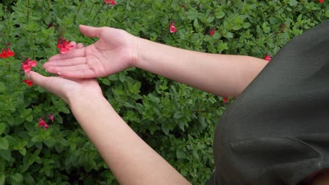 fair skin lady reaches to touch flower in nature, green dress, over shoulder