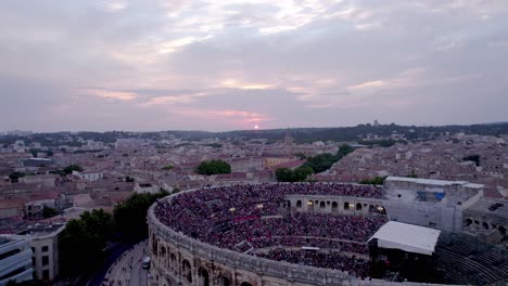 Drone-to-move-back-over-the-Arena-of-Nimes-at-sunset,-people-are-waiting-for-the-stromae-concert