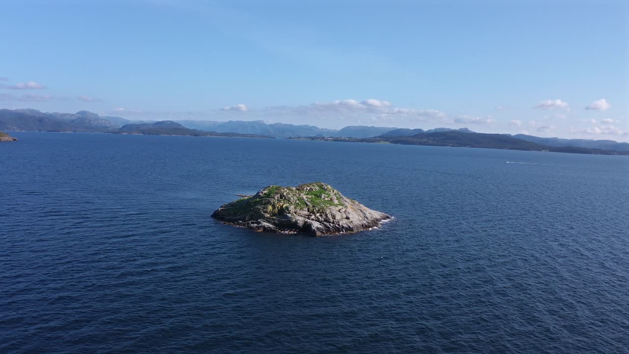 A small rocky island in the ocean, surrounded by clear blue waters in norway, aerial view