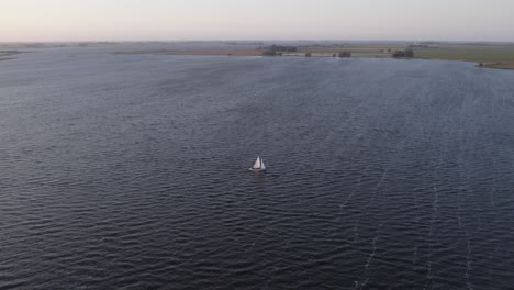 Orbit-around-sailing-boat-cruising-on-lake-Fluessen-during-sunset,-aerial