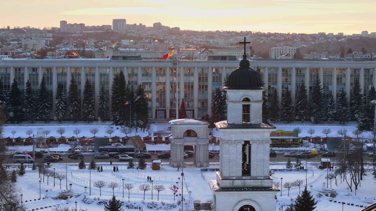 Aerial drone view of golden crosses on top of the Bell tower and the Metropolitan Cathedral of Christ's Nativity at sunset. Government House of Moldova in background. Chisinau city covered in snow