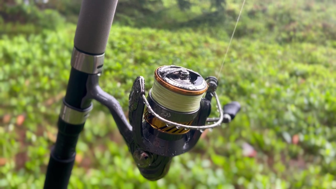 Close-up of a fishing reel covered with water droplets above coastal heather.