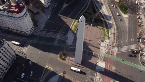 aerial top down shot of bus driving on road around obelisk monument in buenos aires