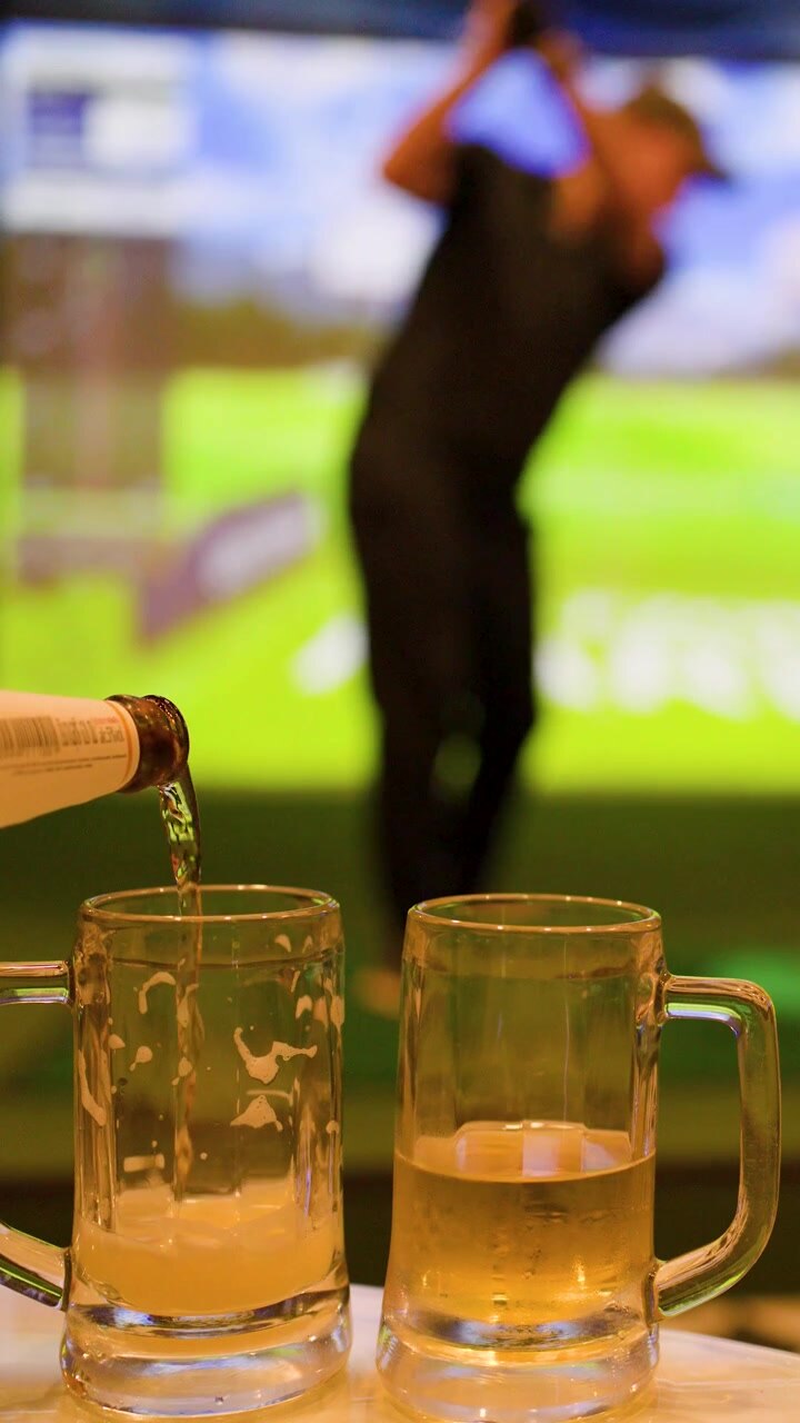 Un uomo colpisce una pallina da golf in un simulatore mentre la birra riempie un boccale di vetro.