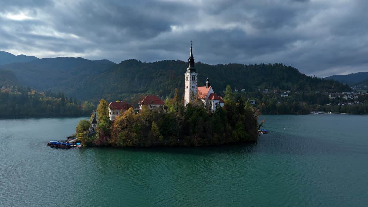 Orbita di drone attorno alla Chiesa di Pellegrinaggio dell'Assunzione di Maria sull'isola di Bled. Scenografica luce mattutina sul lago turchese e montagne nebbiose in Slovenia.
