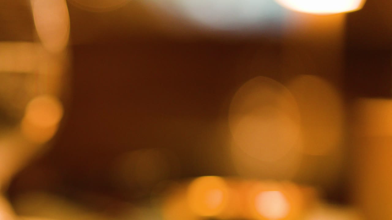 A hand lifts a cocktail glass with ice from a warmly lit bar counter, evening ambiance