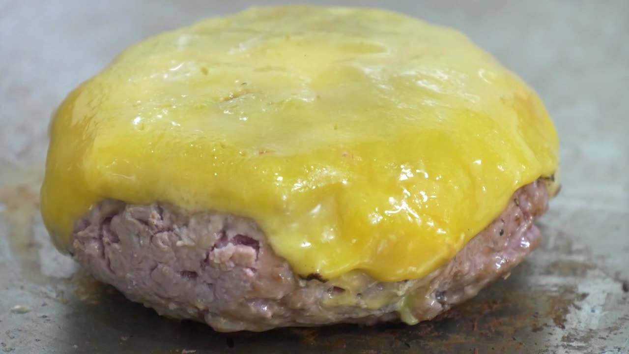 primer plano de una hamburguesa con queso ligeramente rosada todavía en la parrilla