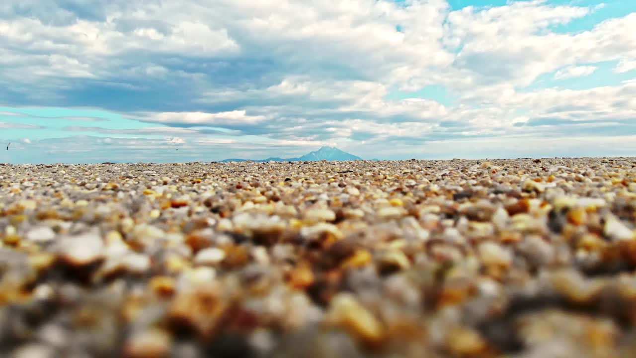 View of a beach from the ground. Sand, clouds, mountain in the distance, Greece