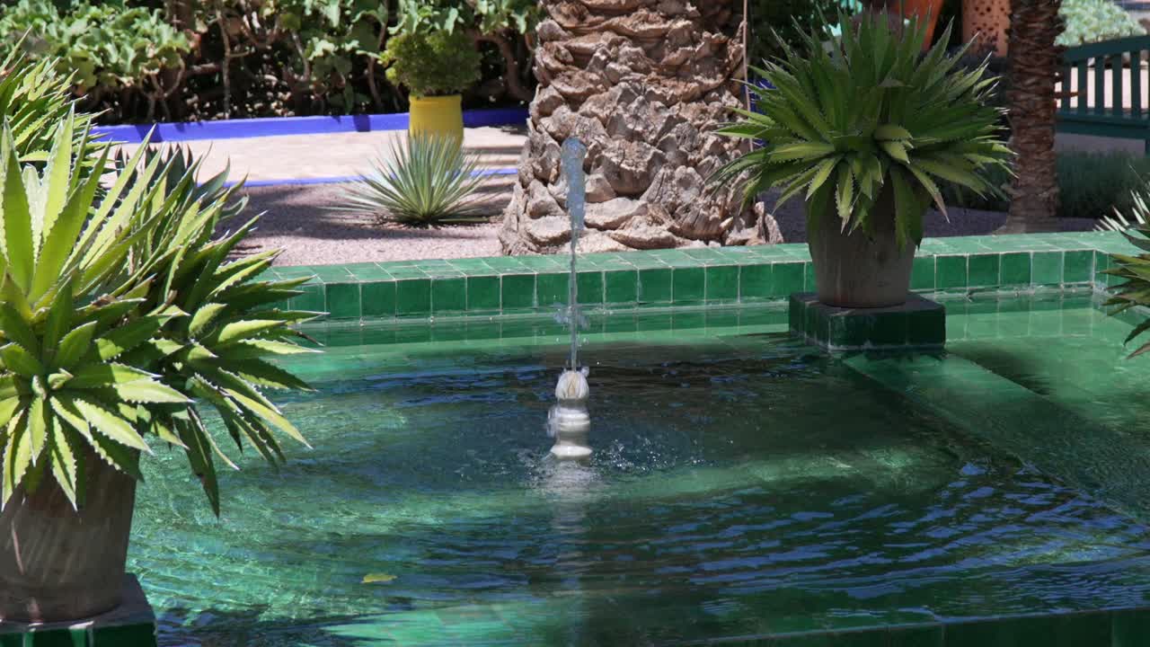 Beroligende havefontæne i Jardin Majorelle, Marokko, under skarpt sollys.