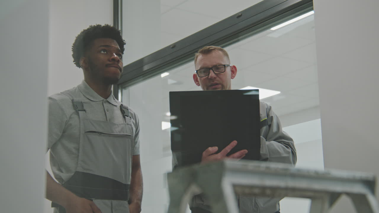 Two Engineers Discussing Work with a Laptop in a Modern Factory