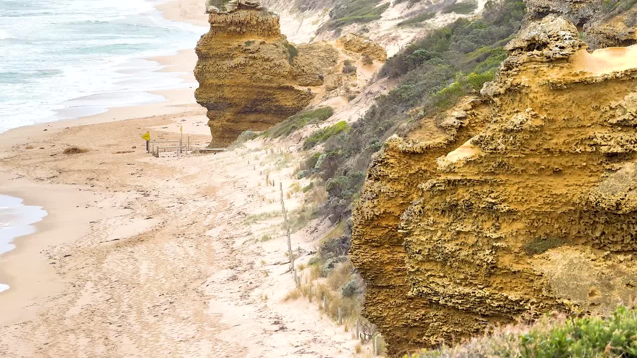 A serene beach walk beside towering cliffs and ocean waves on a sunny day at Great Ocean Road, Australia