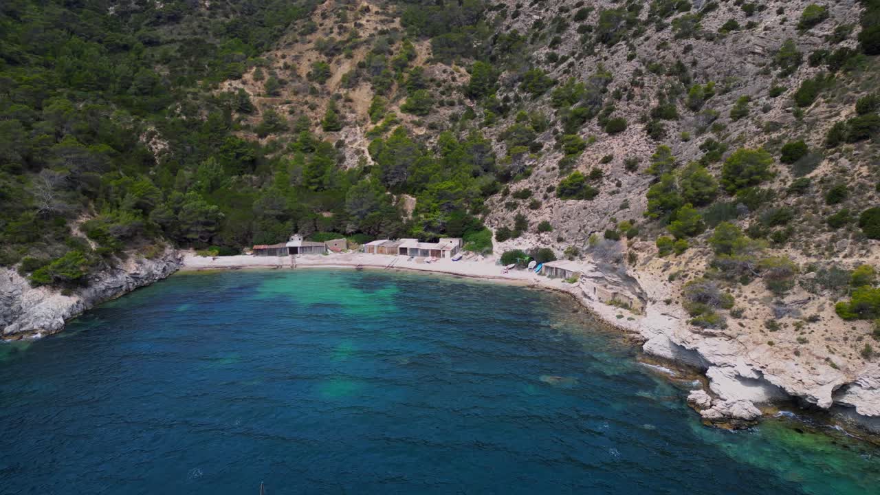 Cala Llentrisca beach with turquoise water and Barques de pescadors Huts in Ibiza, Spain, in summer. Magic aerial view flight panorama orbit drone