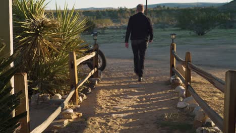 el hombre camina desde la granja de la granja en el desierto para subir a una motocicleta retro chopper y despegar por la carretera al atardecer