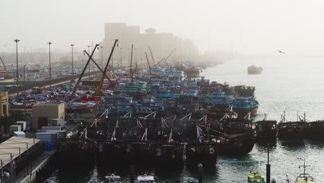 Dhow-Boat-Maneuvering-At-Crowded-Port-In-Dubai-Creek-With-Working-Cranes-in-Dubai,-UAE