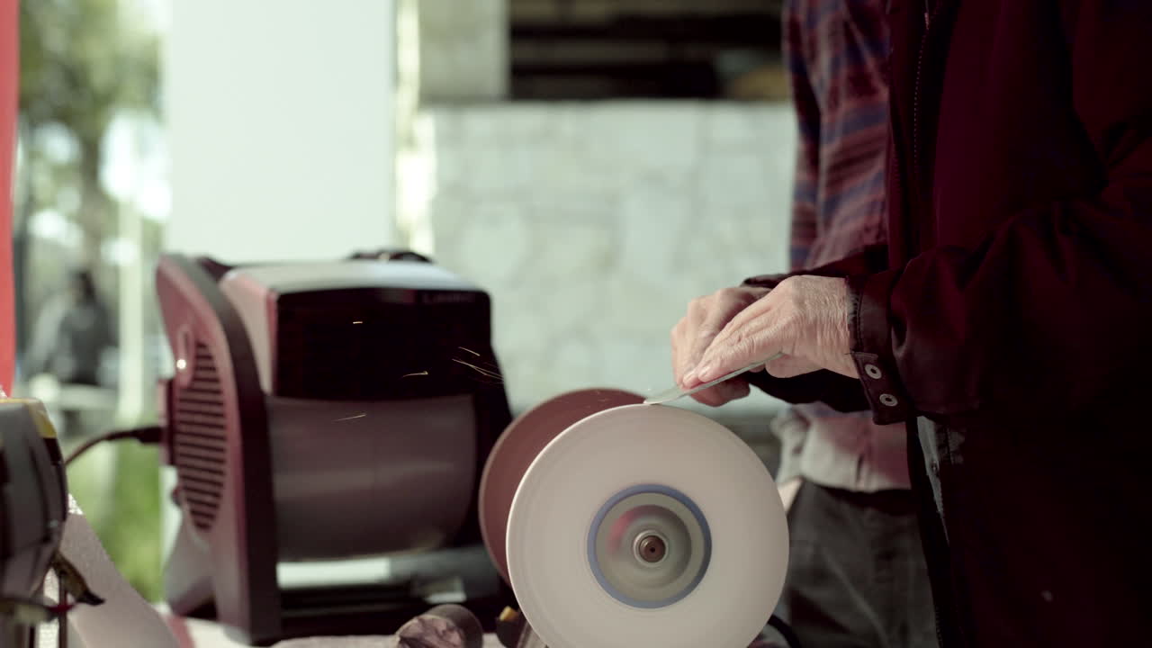 Close-up of Hands Sharpening a Blade on a Grinding Wheel with Sparks