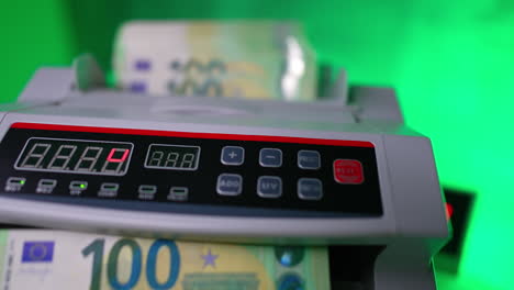 stack of euro bills is put into money counting machine. one hundred banknotes counted in bank device. close up. blurred backdrop.