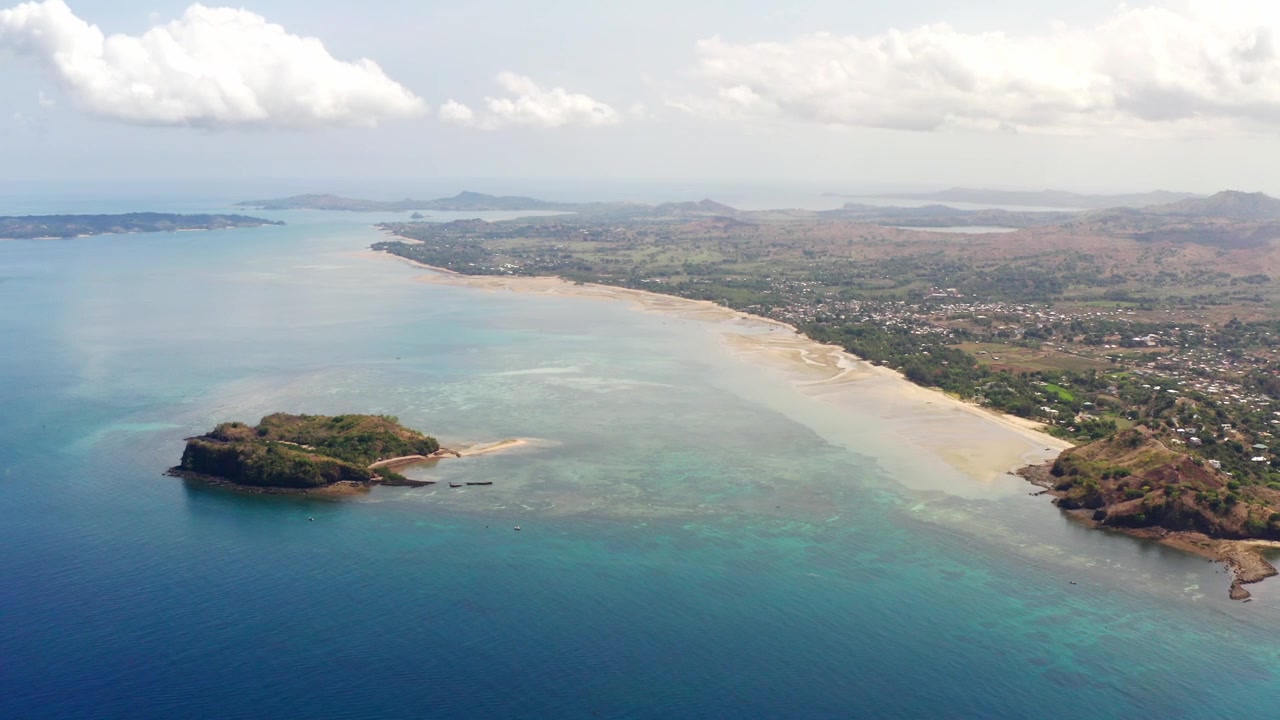 Vista aerea da drone dell'isola di Nosy Be in Madagascar durante una giornata di sole; l'oceano blu e la costa della spiaggia riflettono le nuvole a Palm Beach. L'isola di Nosy Tanga è presente nell'inquadratura.