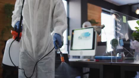 mid section of health worker wearing protective clothes cleaning office using disinfectant sprayer