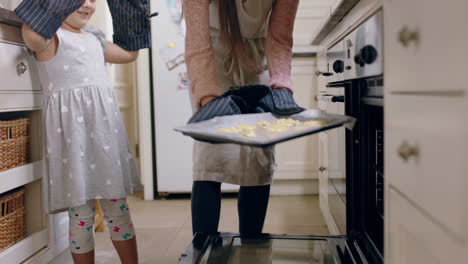 Kleines-Mädchen-Hilft-Mutter-Beim-Backen-In-Der-Küche,-Legt-Selbstgemachte-Kekse-In-Ofenhandschuhe-Und-Genießt-Frische,-Köstliche-Leckereien