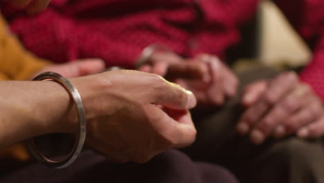 primer plano de una familia sikh masculina de varias generaciones usando y discutiendo brazaletes o pulseras tradicionales de plata sentados en el sofá en casa 1