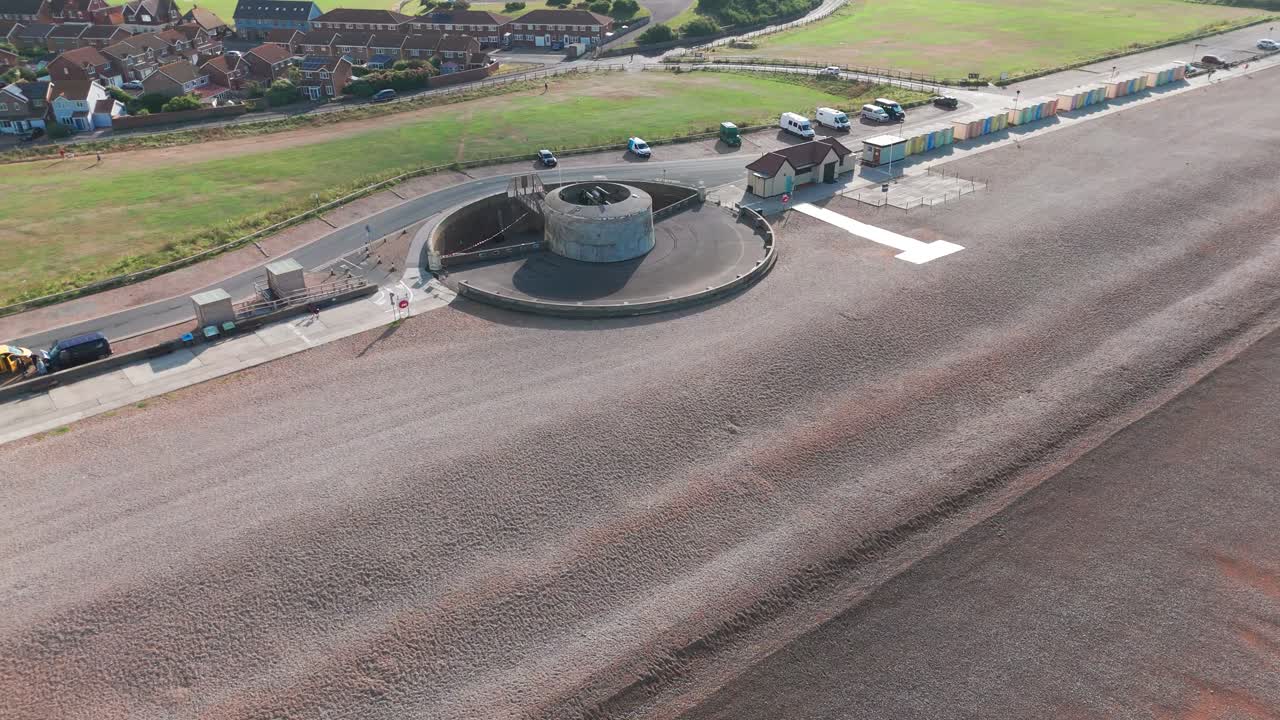 Aerial View of a Shingle Beach with Beach Huts, Concrete Structure, and Coastal Town