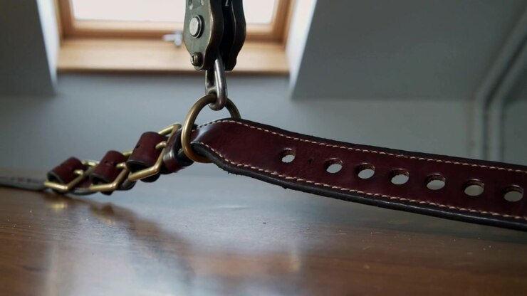 Sliding brown leather strap shifting from D-ring contact across table under skylight with buckles