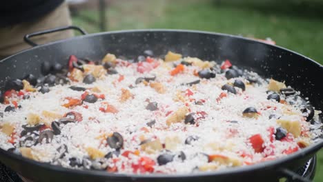 Close-up-of-a-paella-being-cooked-and-rice-being-pored-on-top-of-it-with-spices