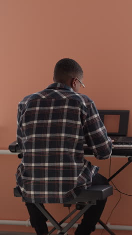 student entertains with synthesizer at home. african american instrumentalist practices musical piece using electrical device in well-lit hostel room