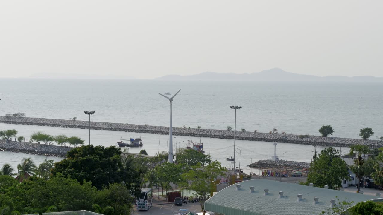 A scenic view of a fishing boat and wind turbines at a tranquil seaside harbor.
