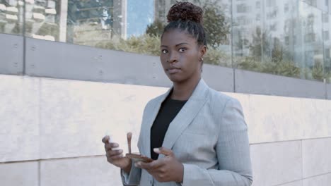 dolly shot of a smiling african-american businesswoman walking outside, holding coffee and using mobile phone