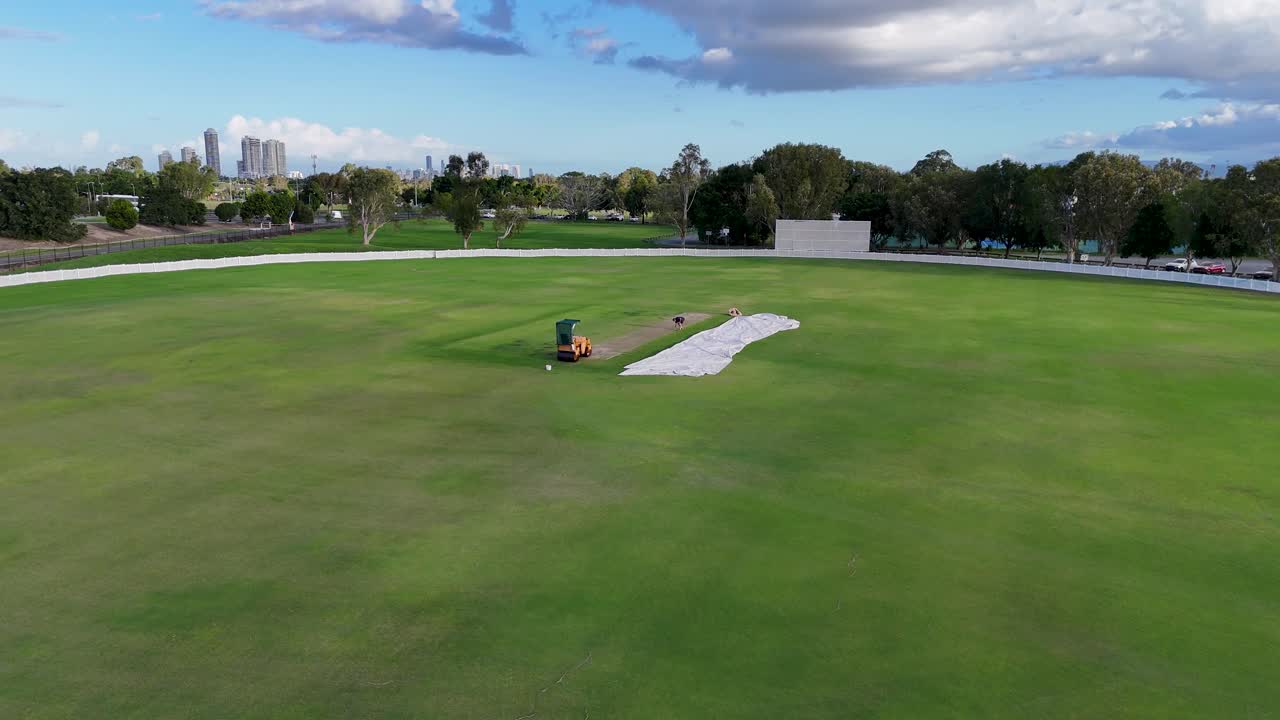 Aerial footage of groundskeepers maintaining a sports field in Gold Coast, Australia, under clear skies with lush greenery