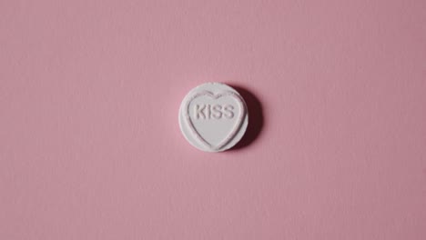 mano recogiendo caramelos de corazón con beso de palabra sobre fondo rosa