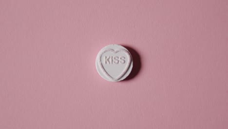 hand picking up heart candy with word kiss on pink background