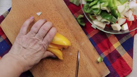 Vista-Aérea-De-Las-Manos-De-La-Mujer-Usando-Un-Cuchillo-Para-Cortar-Pimiento-Dulce-Amarillo-En-Una-Tabla-De-Cortar-Y-Agregarlo-A-Un-Tazón